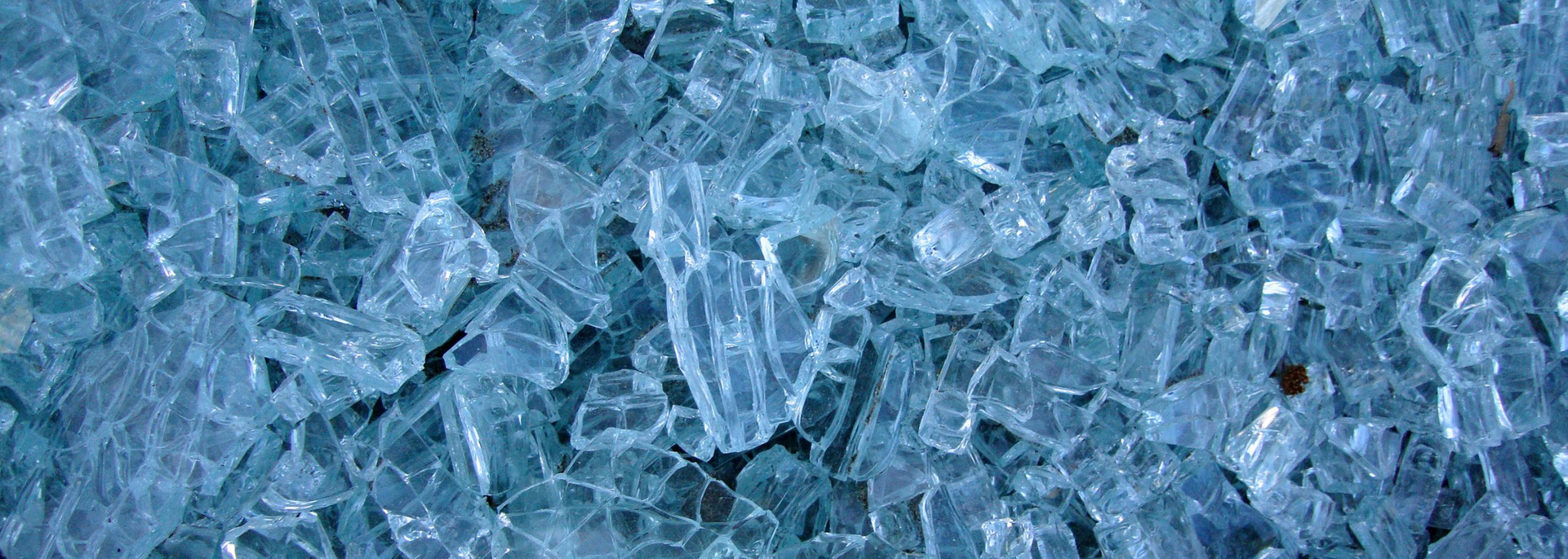 Close-up of a pile of shattered glass, fragments in varying sizes with a light blue hue.