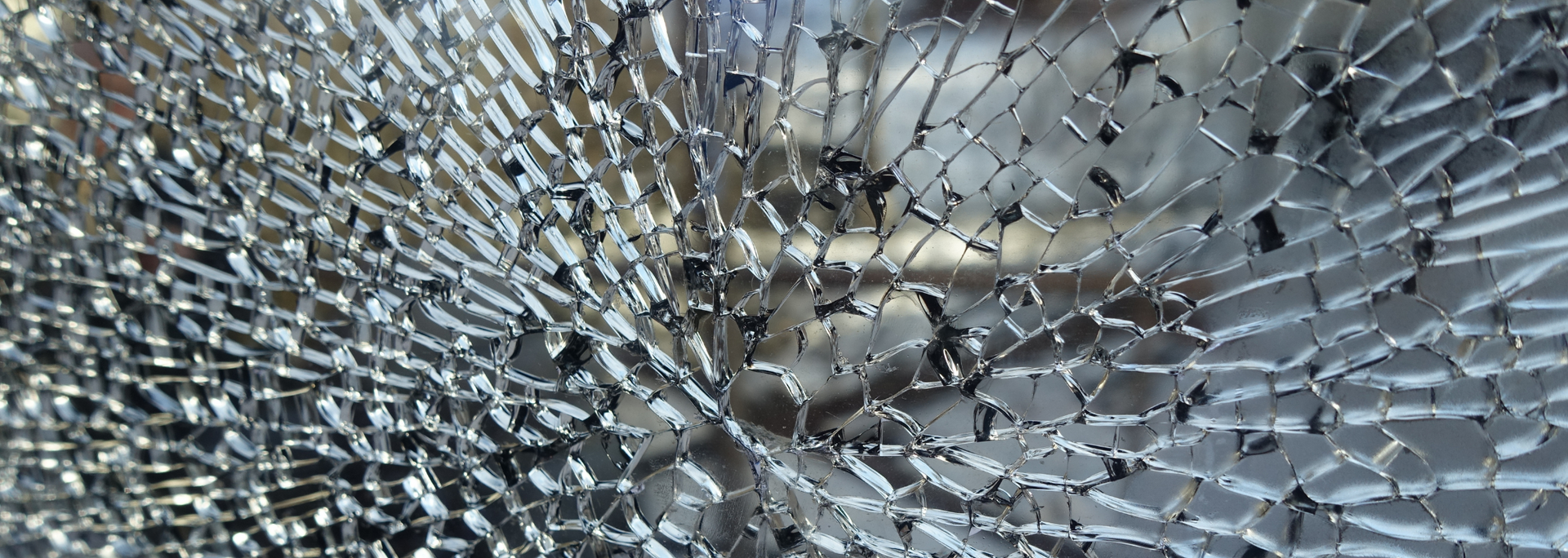 Shattered glass with a web-like pattern of cracks, appearing translucent with reflective light.