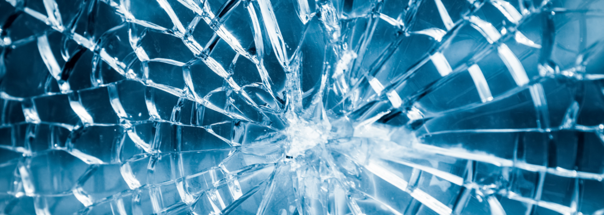 Close-up of a shattered glass pane, radiating cracks from a central impact point, in blue hues.