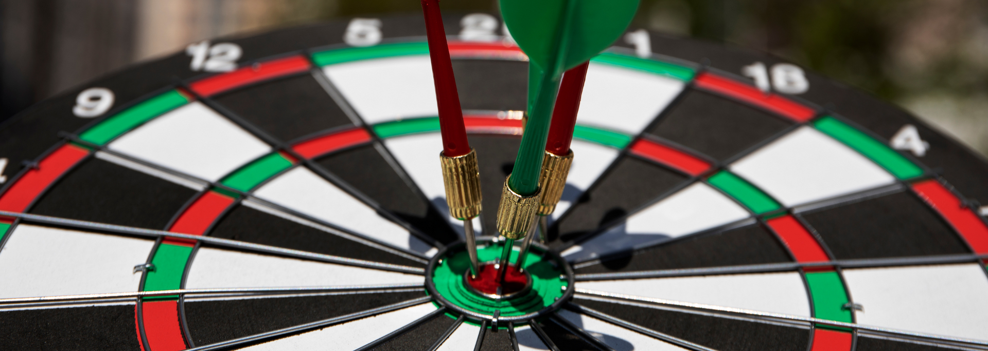 Dartboard with three darts, two red and one green, hitting the bullseye.