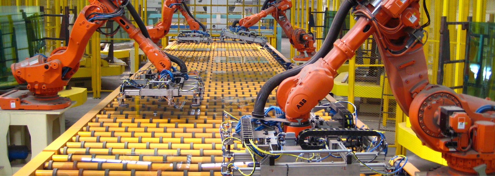 Industrial robots on an assembly line, orange arms working on products, yellow and green industrial setting.