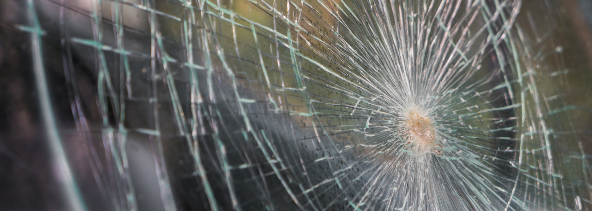 Shattered glass with cracks radiating from a central point, revealing a blurred background.