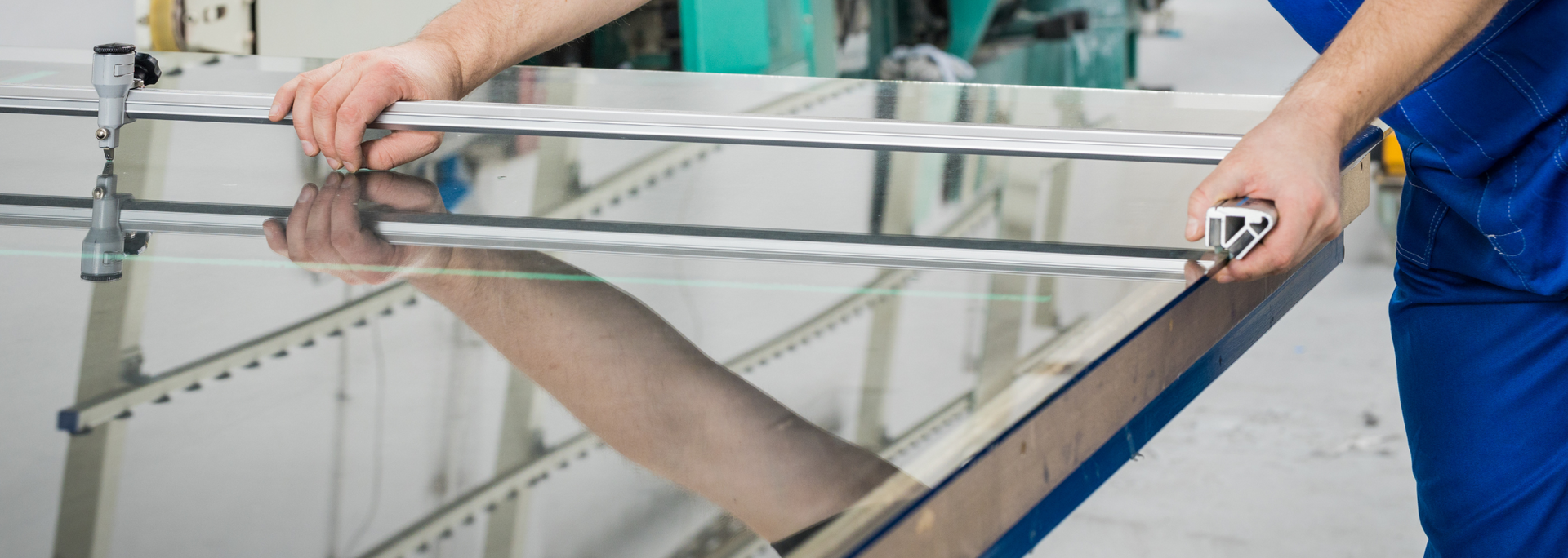 A person measures a reflective surface with a metal measuring tool. They are in a manufacturing setting.