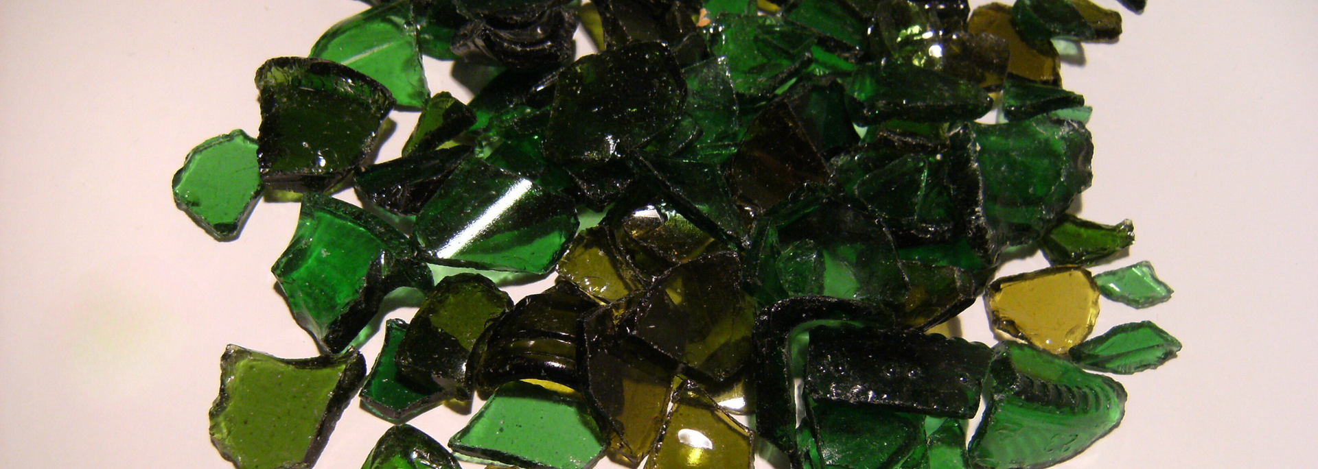Pile of green and olive-colored broken glass pieces on a white background.