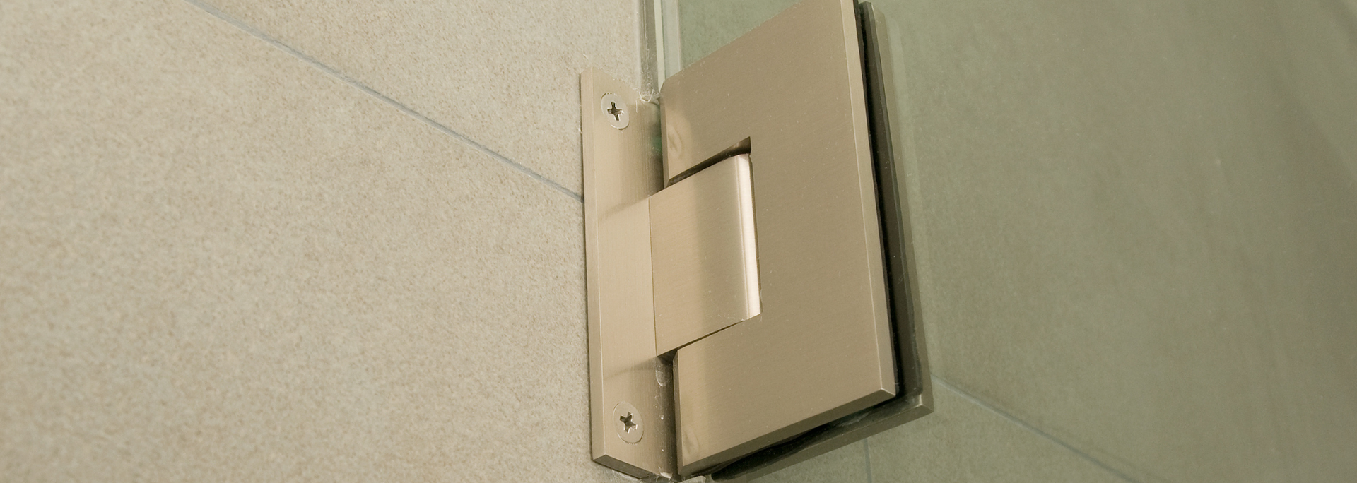Silver hinge attached to a beige wall and a glass panel.