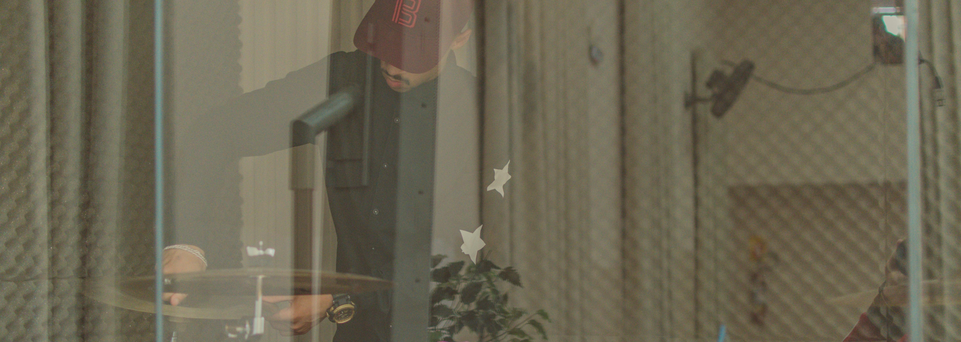 View through glass, showing a room with a curtain, potted plant, and wall fan.