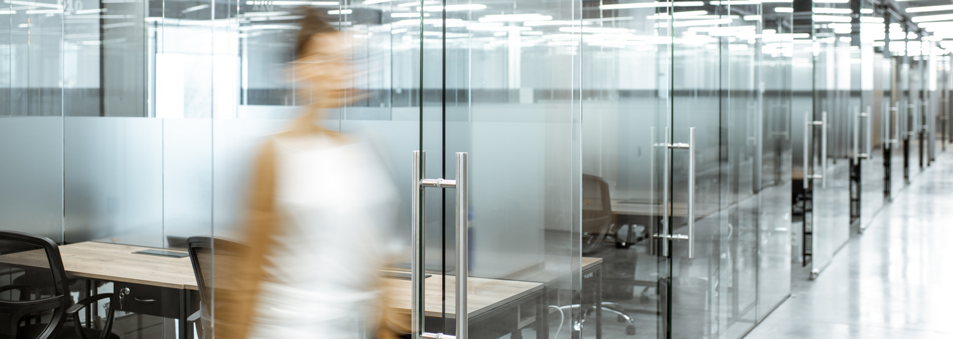 Blurred person walks through an office corridor with glass walls and doors.