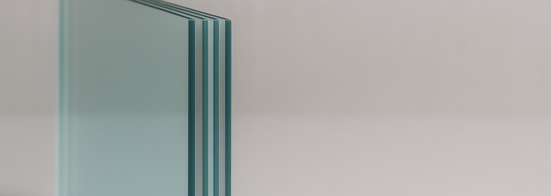 Close-up of a stack of clear glass panels, with light reflecting off the edges, set against a neutral background.