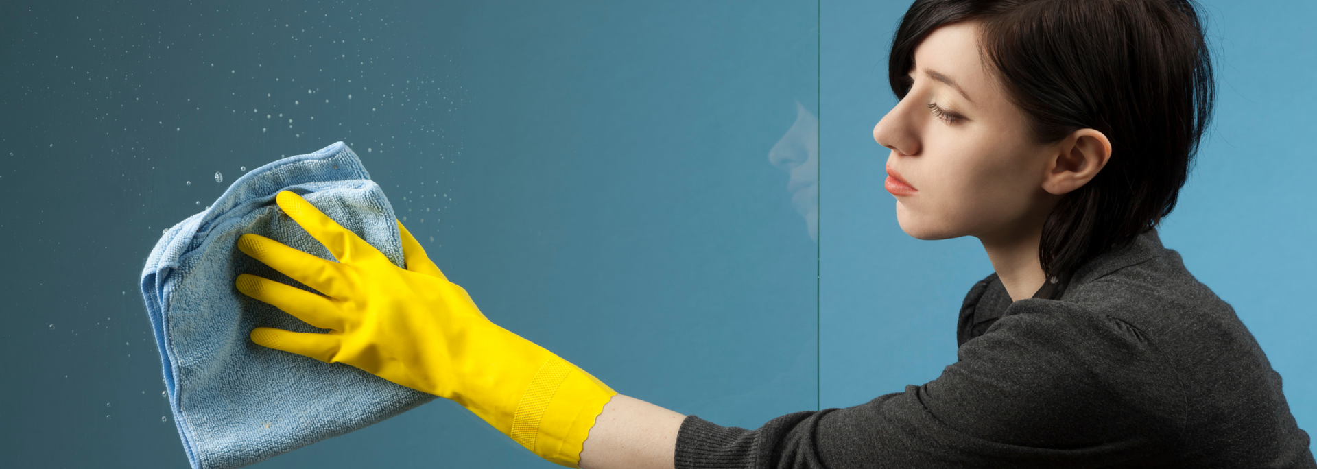 Woman wearing a yellow glove wiping a blue surface with a blue cloth.