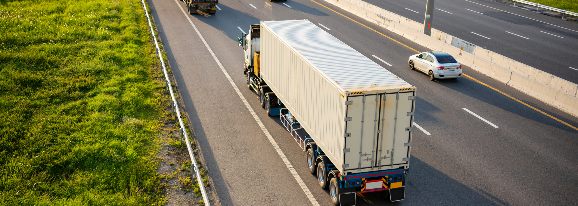 Semi-truck on a multi-lane highway, traveling alongside green vegetation.