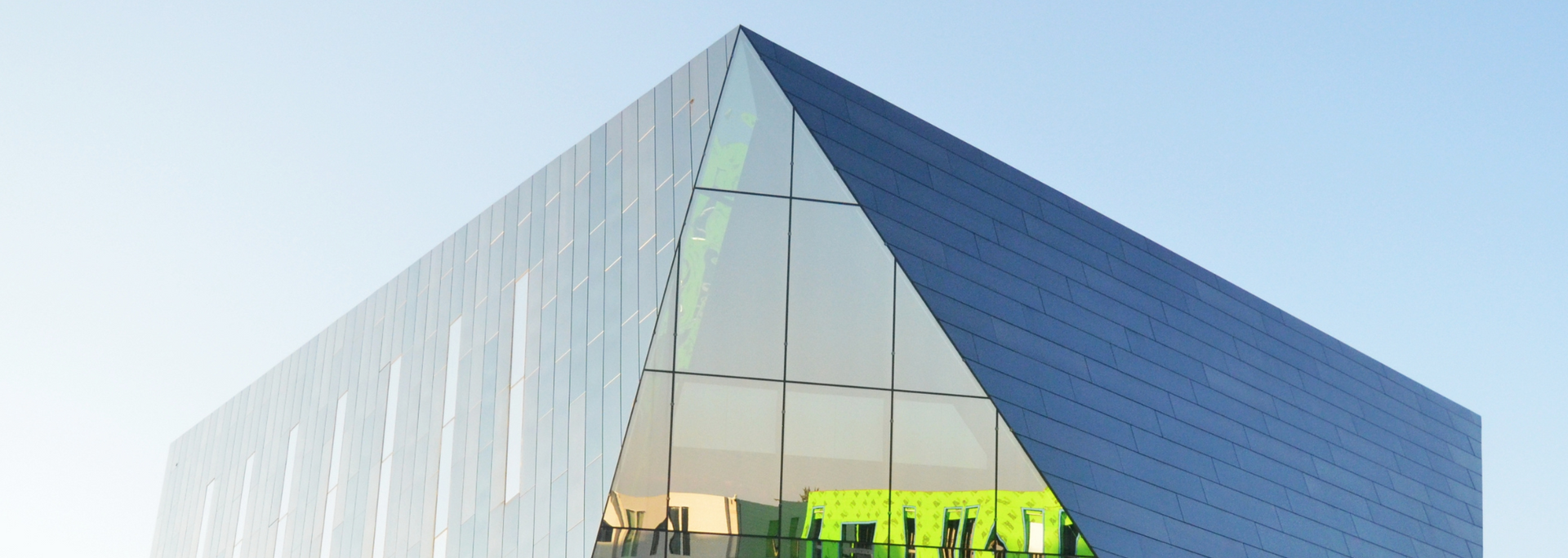 Modern building with triangular glass and blue exterior against a light blue sky.