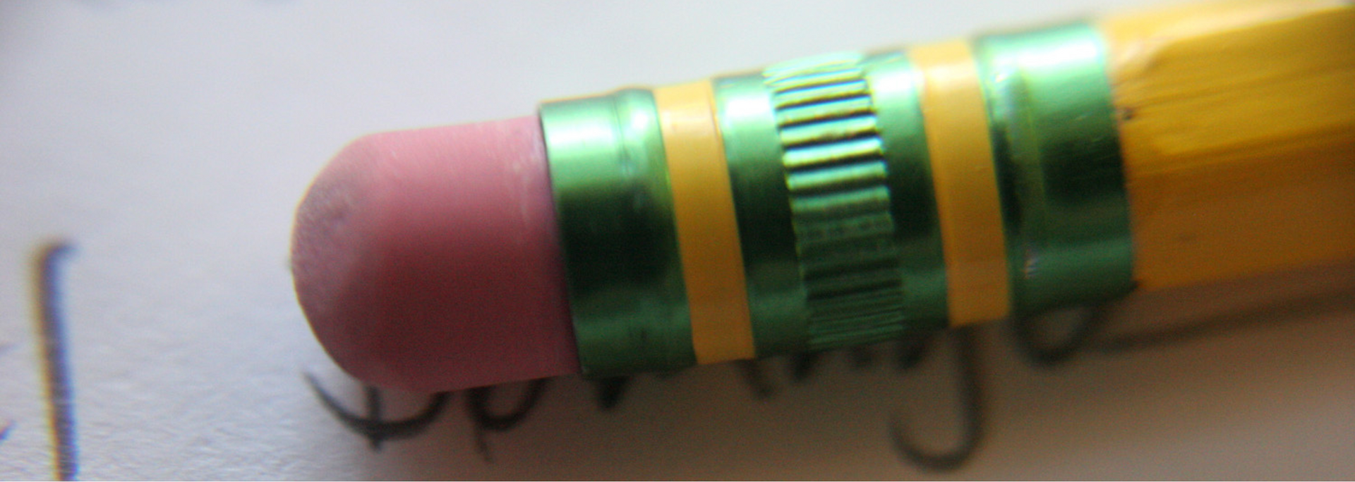Close-up of a pencil eraser with green and yellow bands. Pink eraser tip on a white surface.