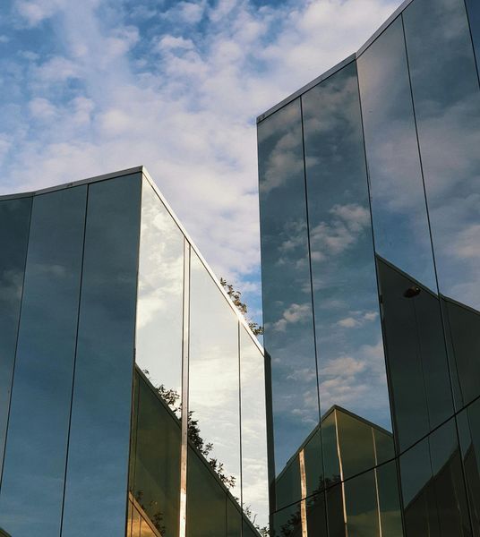 Modern building with reflective glass exterior mirroring blue sky and clouds.