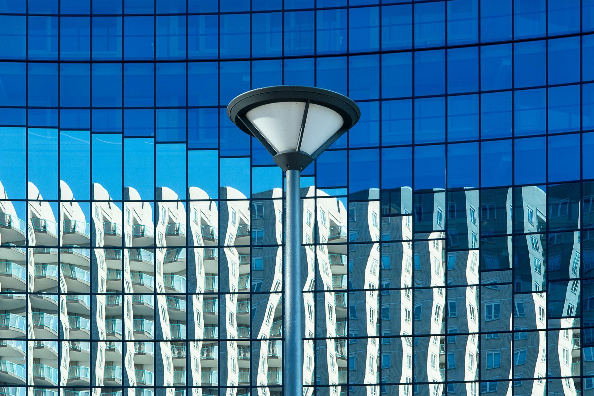 Street lamp in front of a blue glass building, reflecting another building's facade.