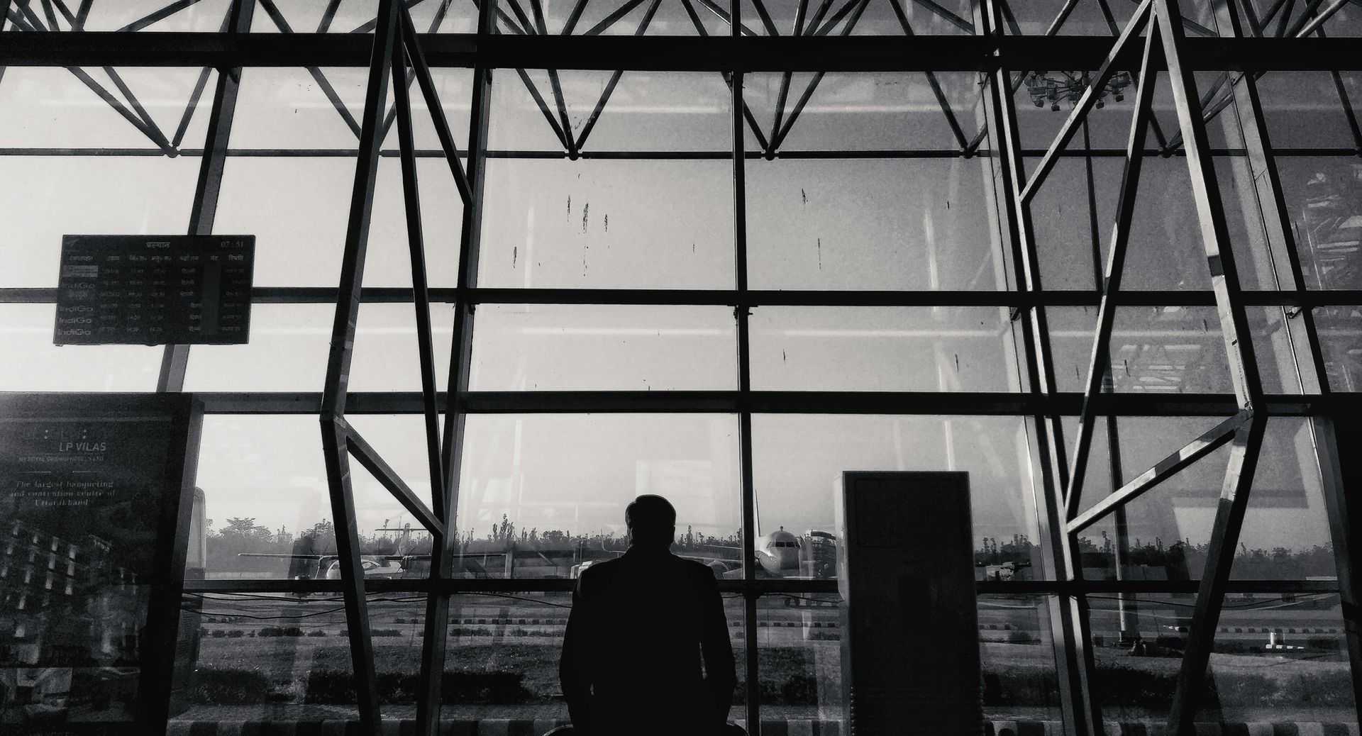 Silhouette of a person inside a building with a large window, facing a bright outdoor view.