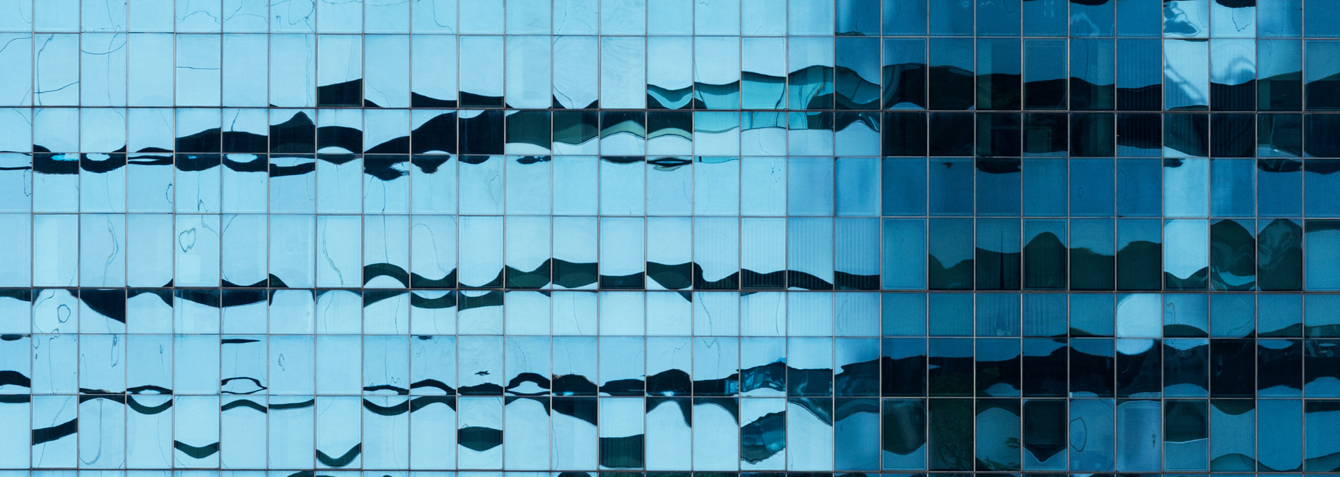 Blue glass building facade reflecting sky and surrounding buildings.