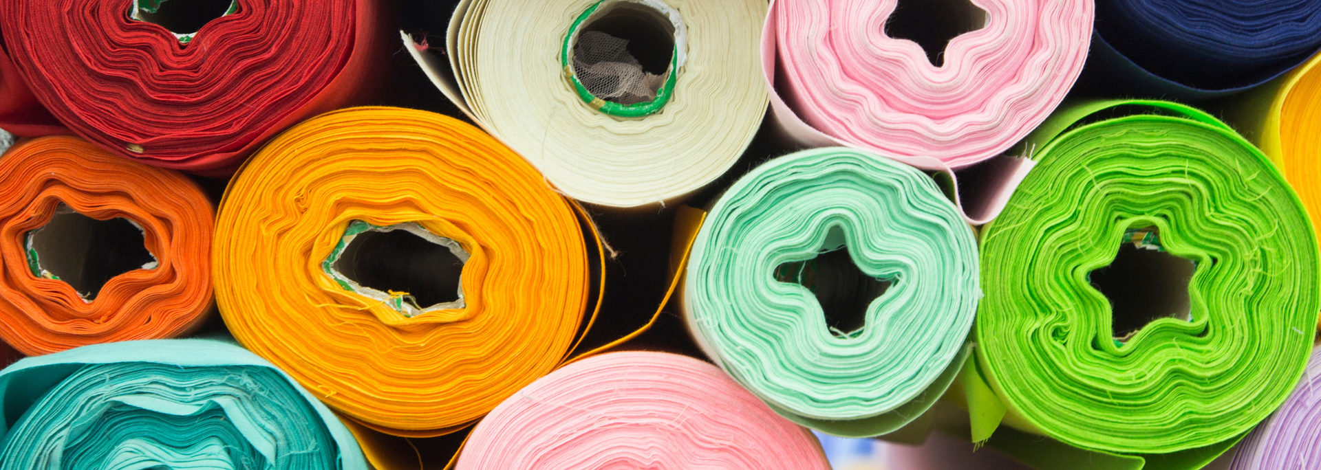 Colorful rolls of fabric, in shades of red, orange, green, and pink.