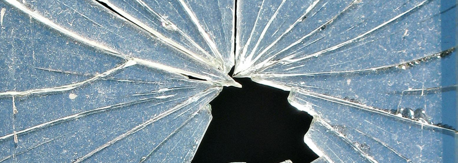 Cracked glass with a large hole in the center, radiating cracks on a blue background.