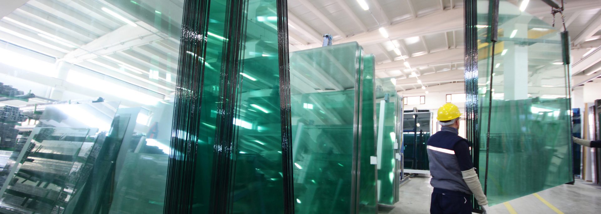Worker in a factory with large sheets of glass. Warehouse setting, bright lights, green tint.