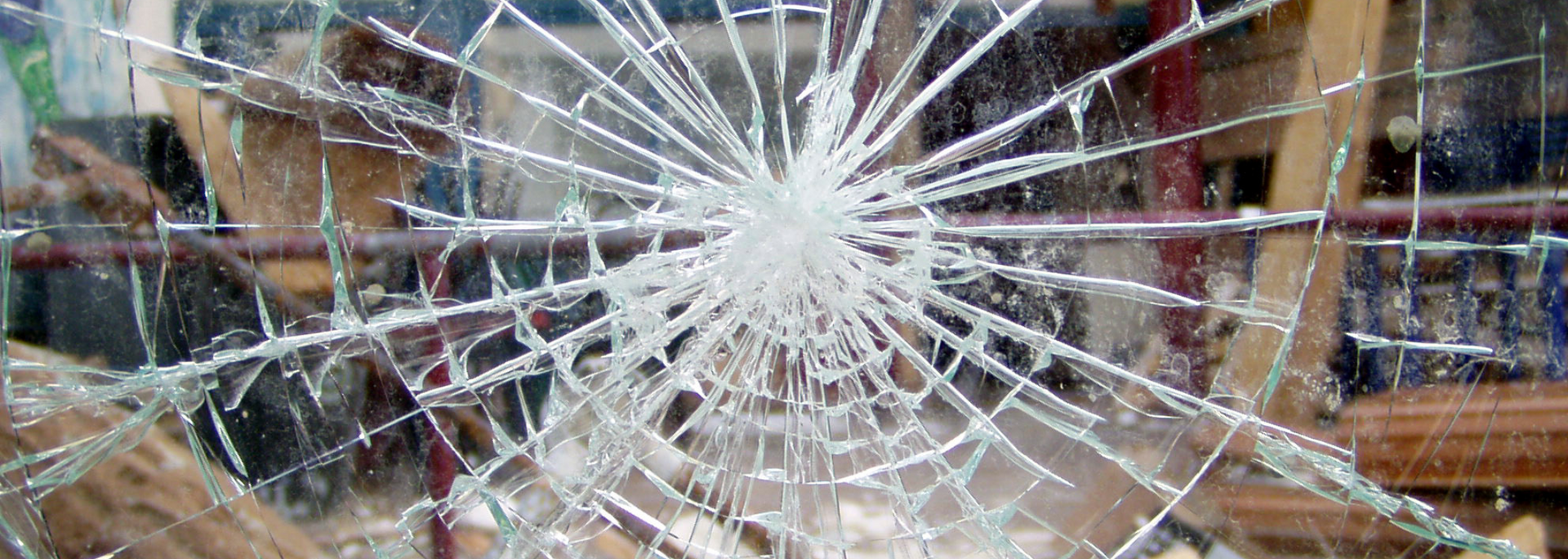 Broken glass with a spiderweb-like pattern. Background reveals blurred shelving.