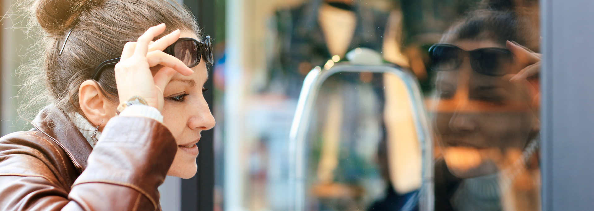 Woman looking at shop window, wearing sunglasses and leather jacket.
