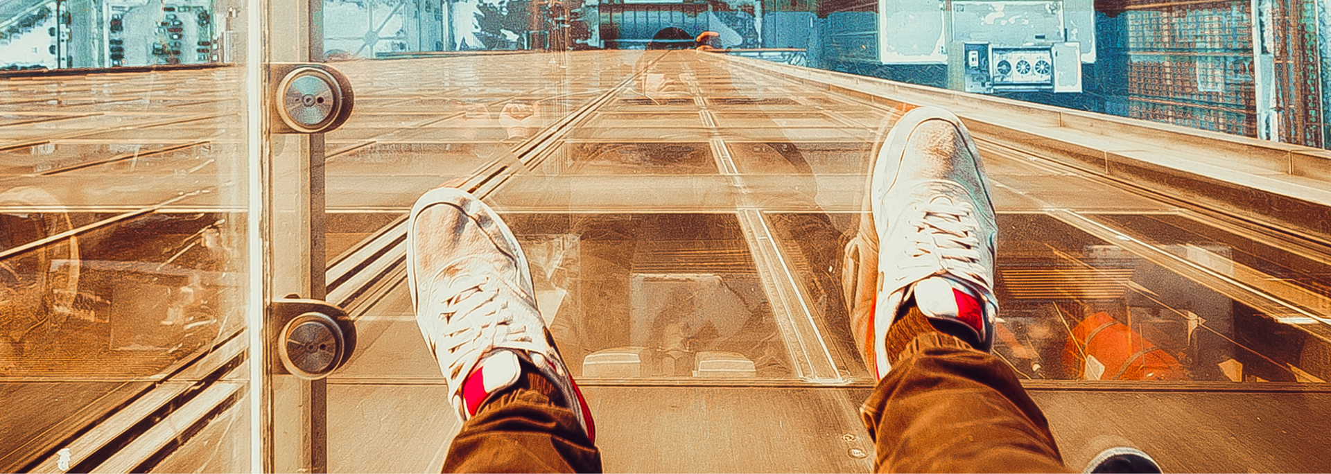 Person looking down at their feet wearing white sneakers with red accents, on a glass floor bridge.