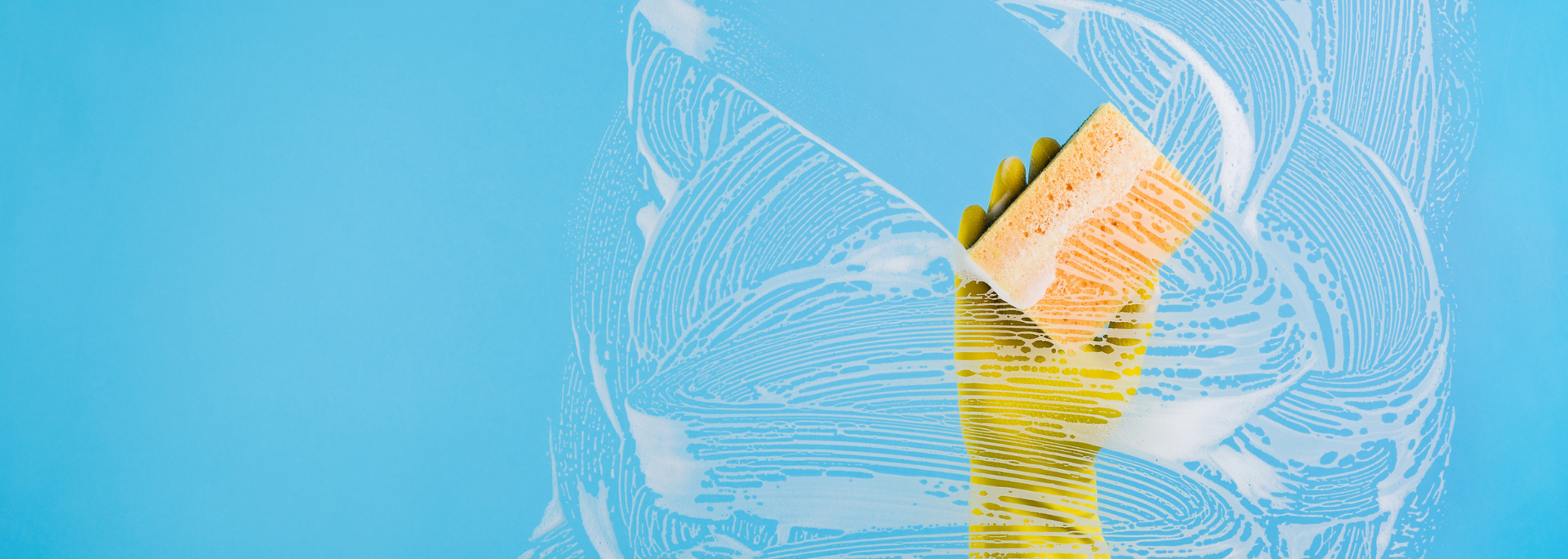 Hand with a yellow glove holding a sponge cleans a soapy blue surface.
