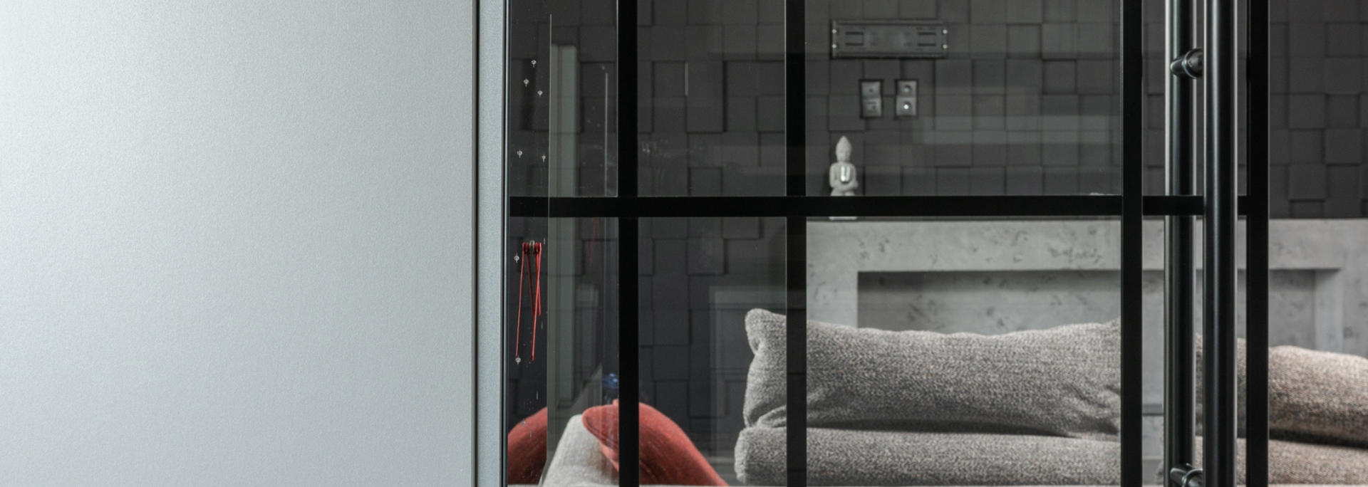 Interior with black-framed glass wall, gray stone backdrop, and pillows.
