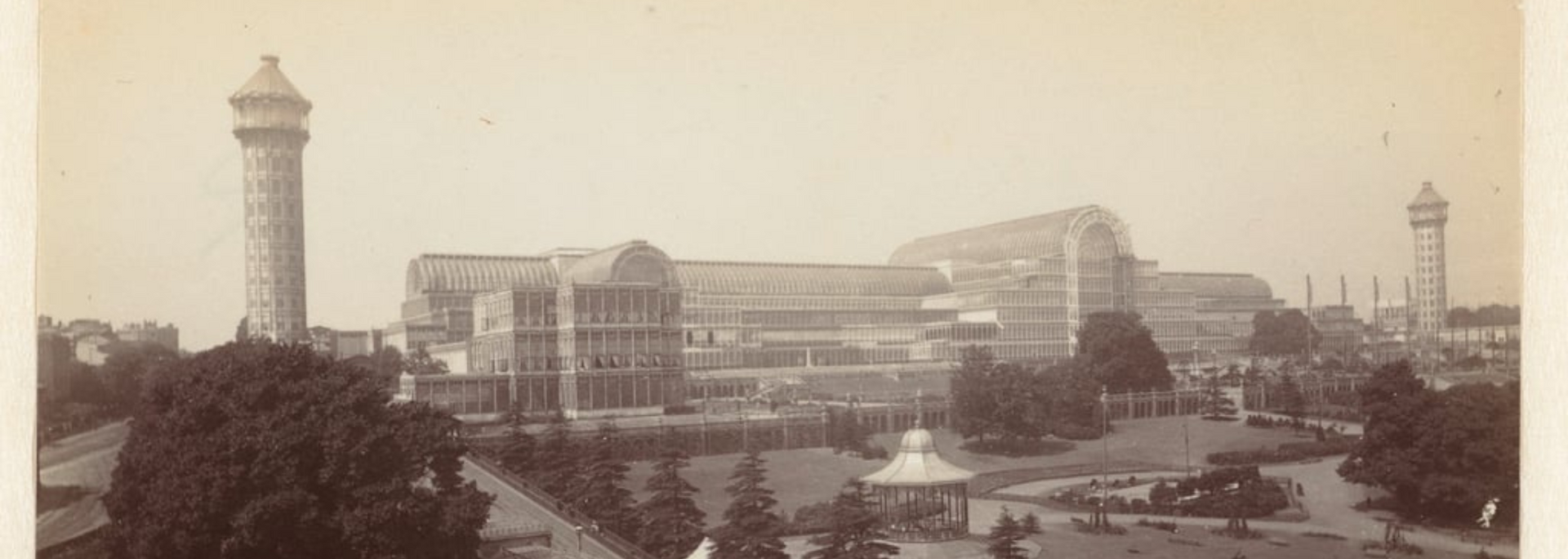 An early sepia-toned photograph of a large, glass-covered building with two tall towers on either side.