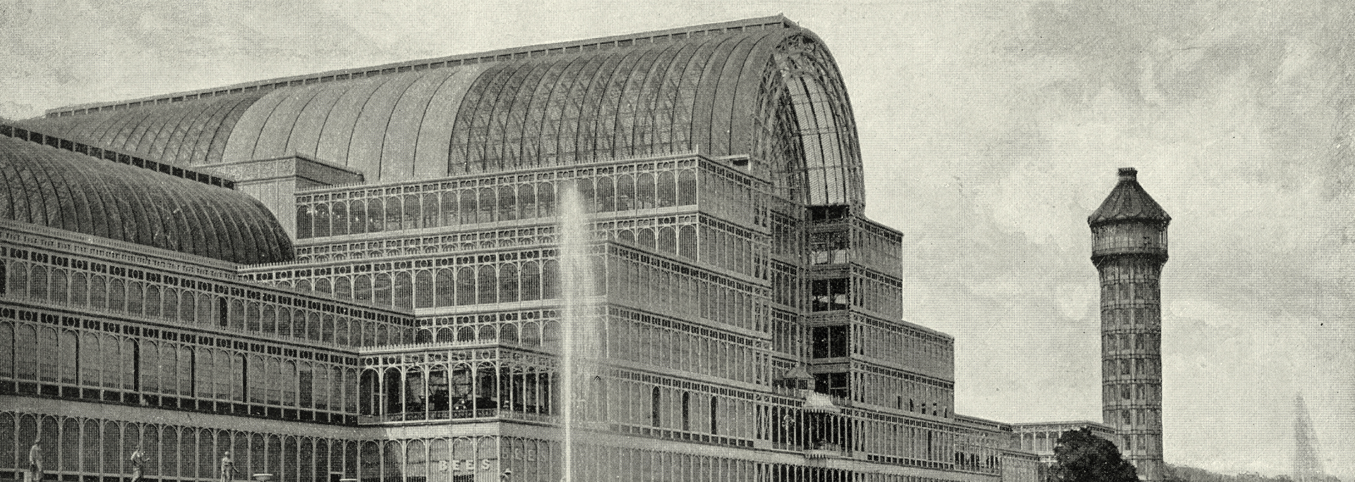 Black and white photo of a large building with a domed roof and a water tower in the background.