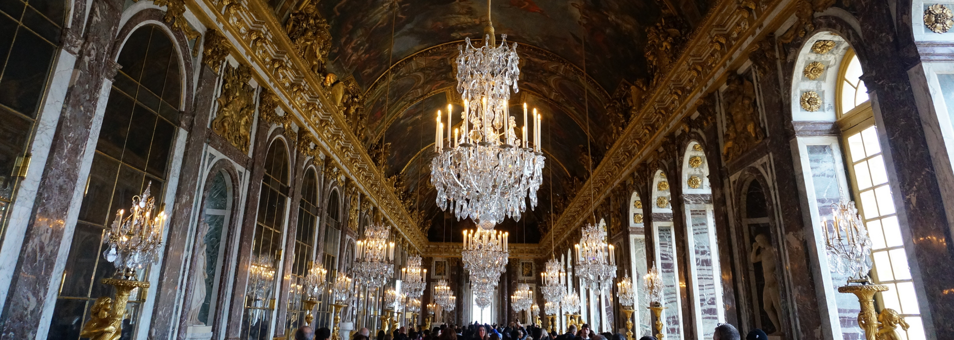 Hall of Mirrors, Palace of Versailles, featuring ornate chandeliers, gilded details, and arched windows.