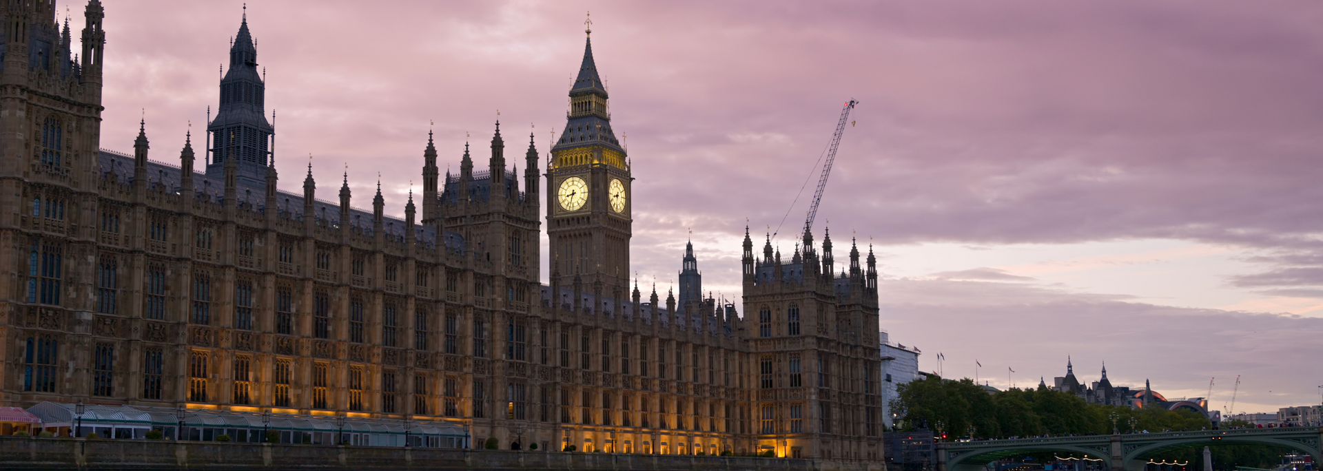 The Palace of Westminster and Big Ben against a pink and purple sky at dusk.