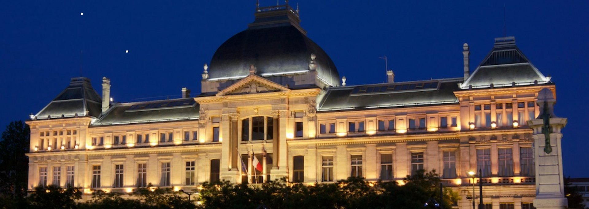 Nighttime view of a grand building with illuminated facades and a large dome, set against a dark blue sky.
