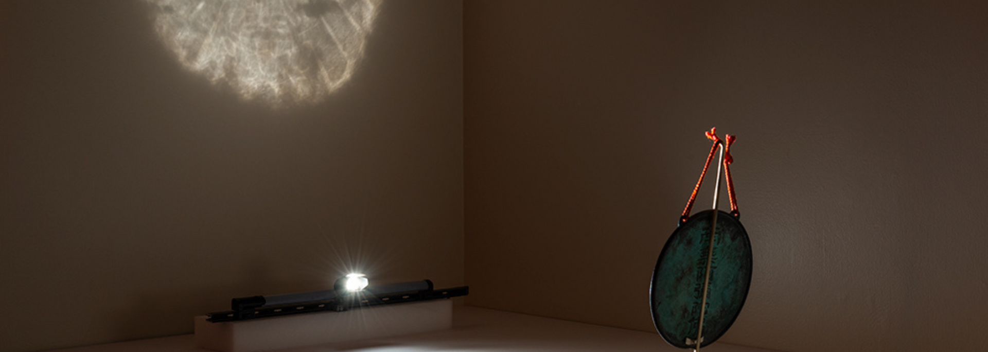 Interior with a dark, leaf-shaped object hanging. Bright light on ceiling and small light on a surface in the room.