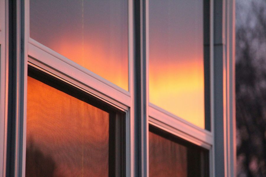 Sunset reflected in a window; orange and yellow sky visible through glass panes, with white frames.