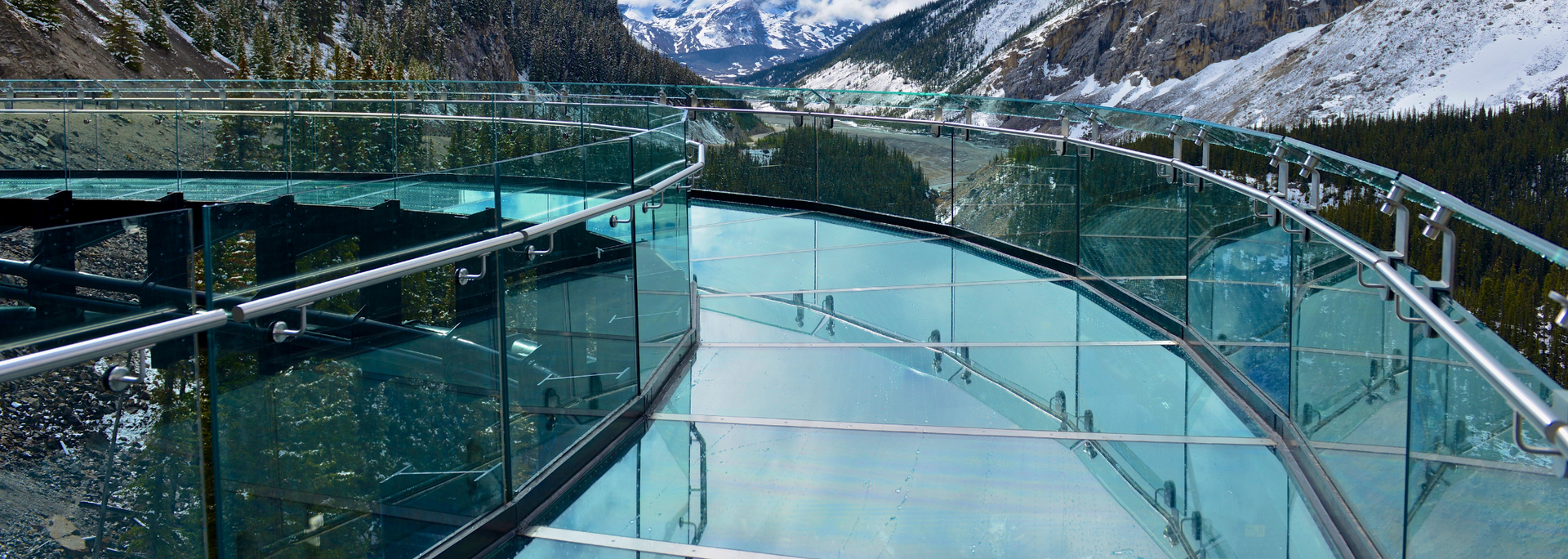 Glass-bottomed walkway overlooking a snowy mountain valley.