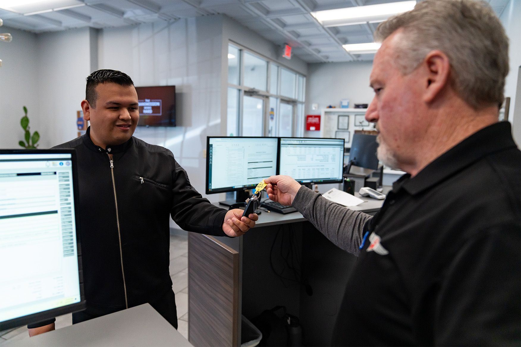 A man is giving a key to another man in an office. | Zia Automotive