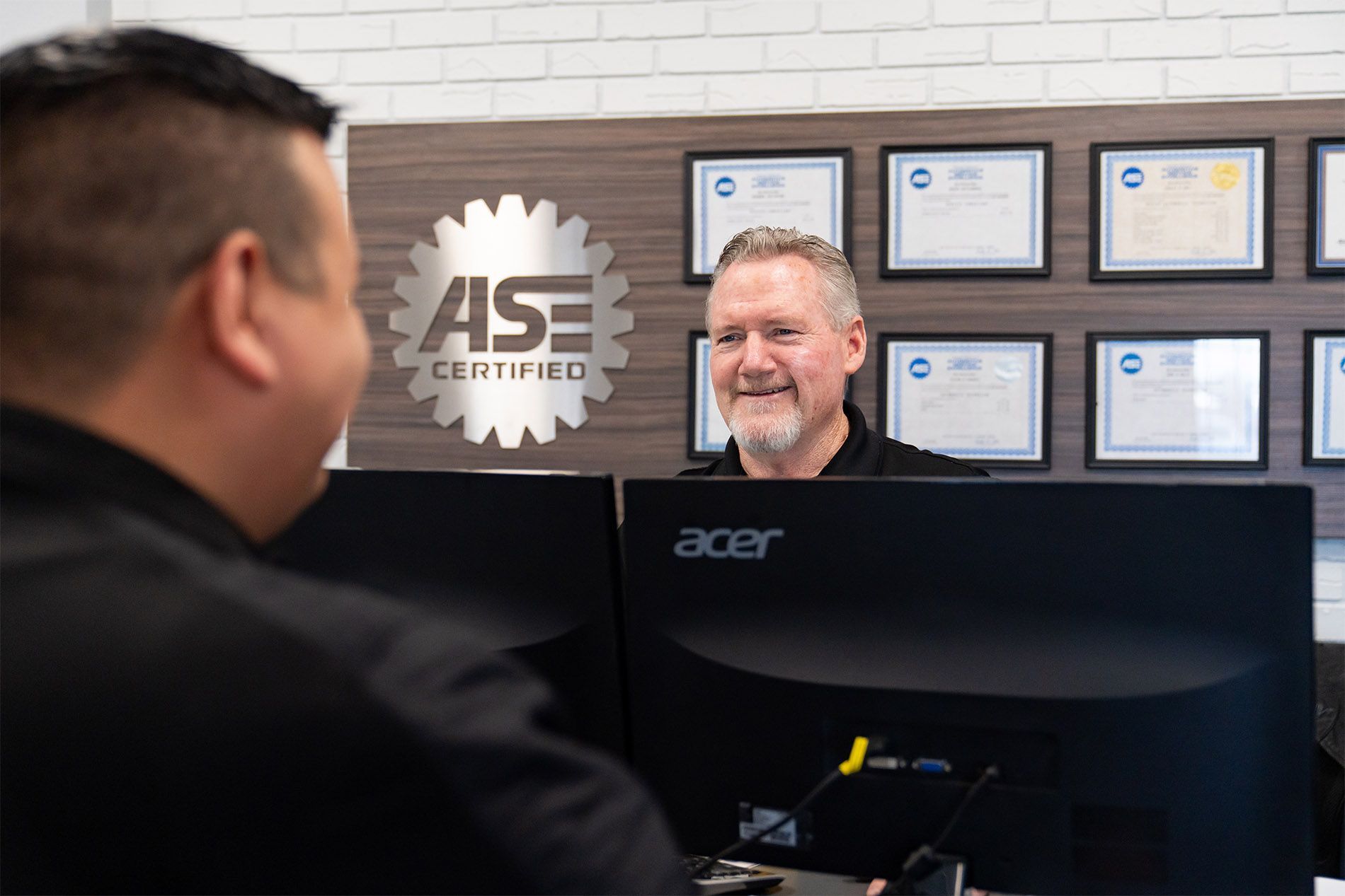 A man is sitting in front of an acer computer talking to another man. | Zia Automotive