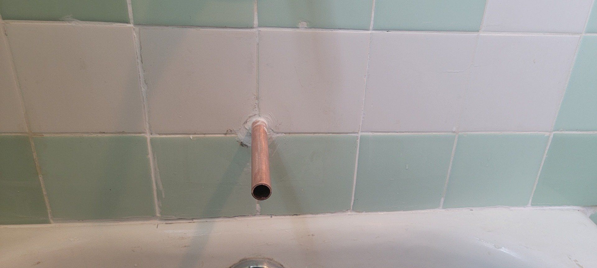 A pipe is sticking out of a hole in a tiled wall next to a bathtub.