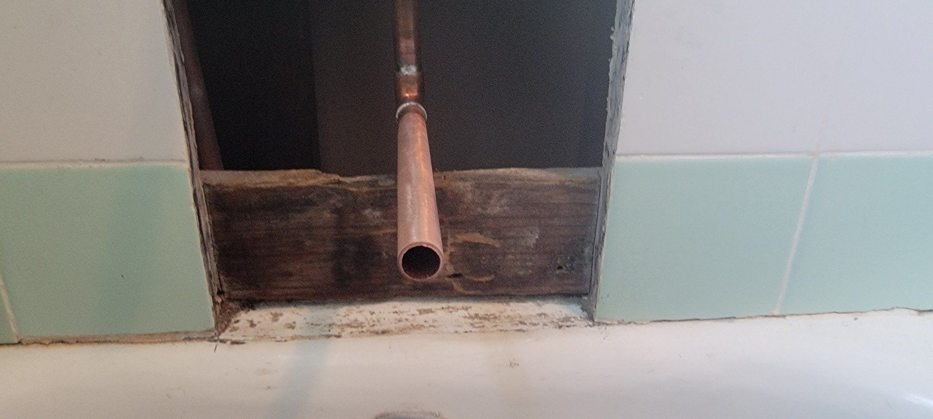 A pipe is coming out of a hole in the wall in a bathroom.