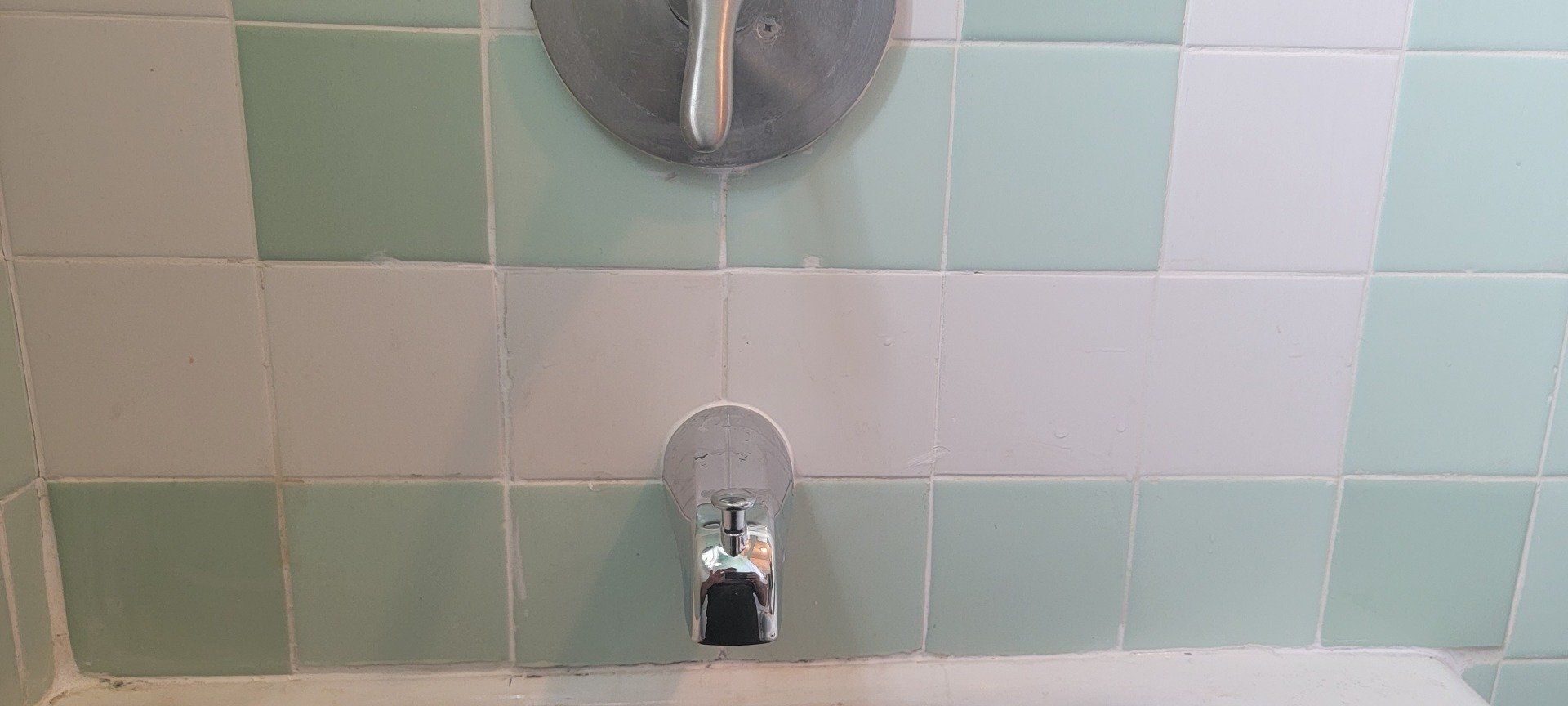 A close up of a shower head in a bathroom with green and white tiles.