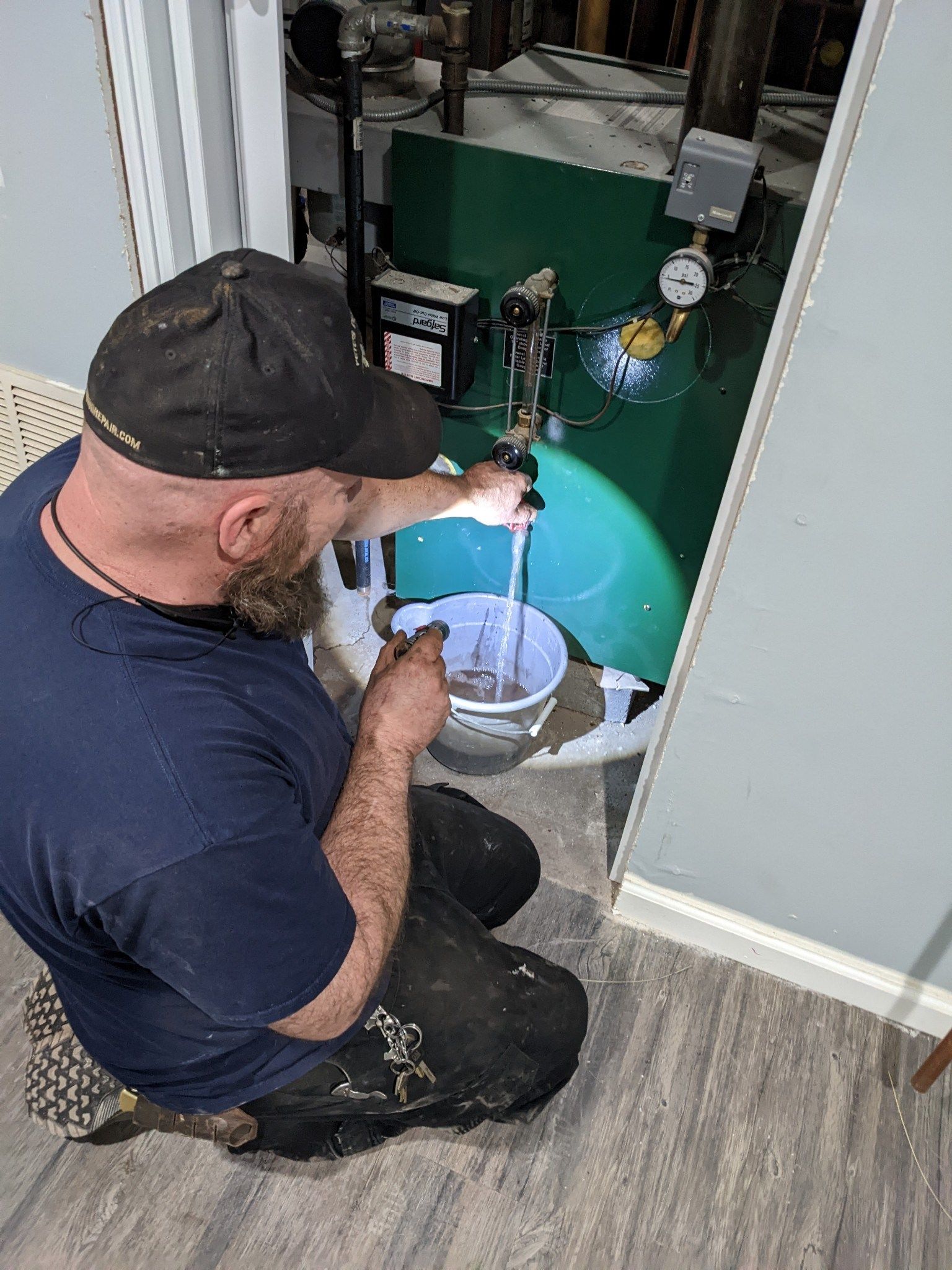 A man is kneeling on the floor looking at a water heater.