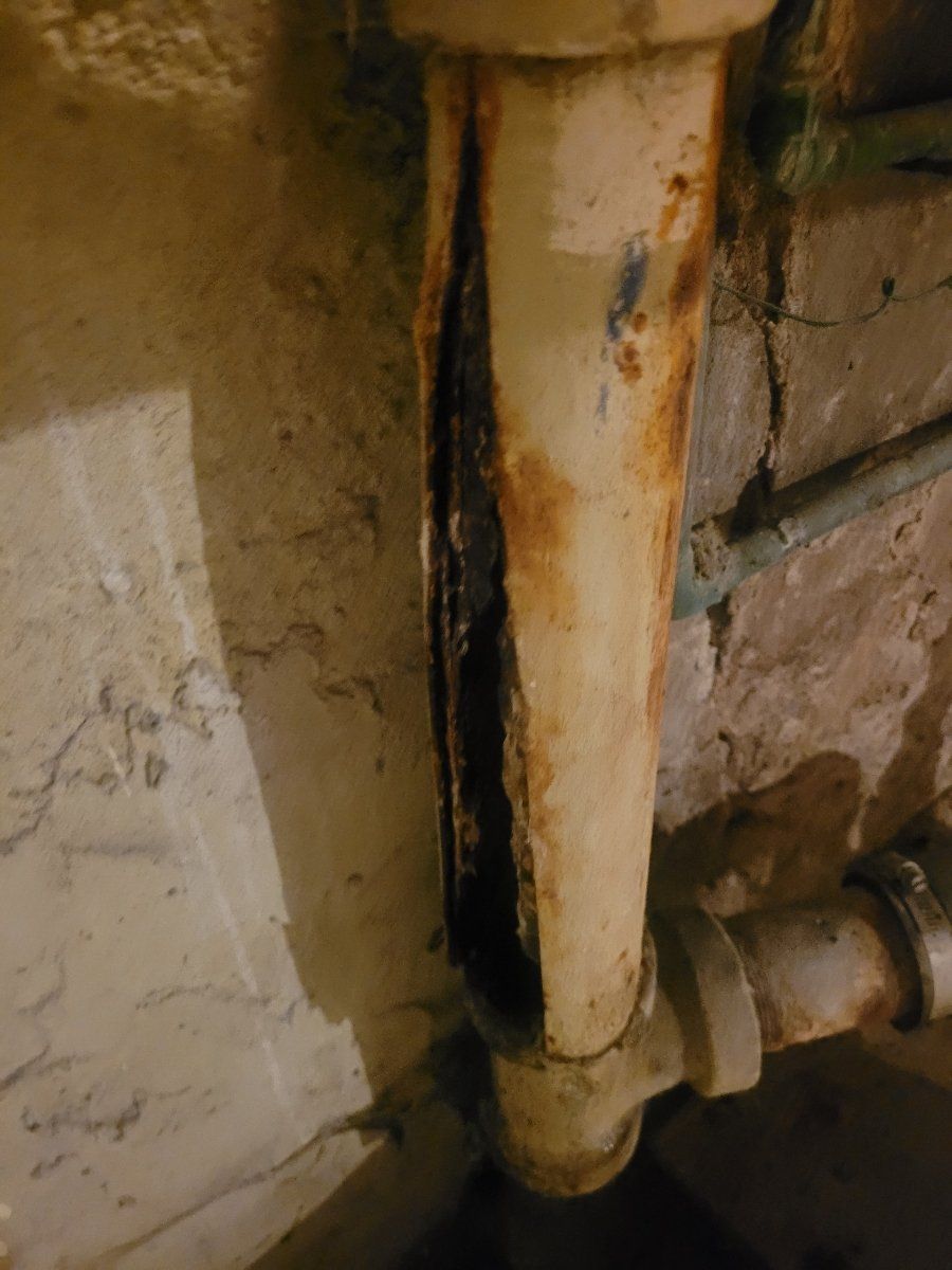 A close up of a rusty pipe against a brick wall.