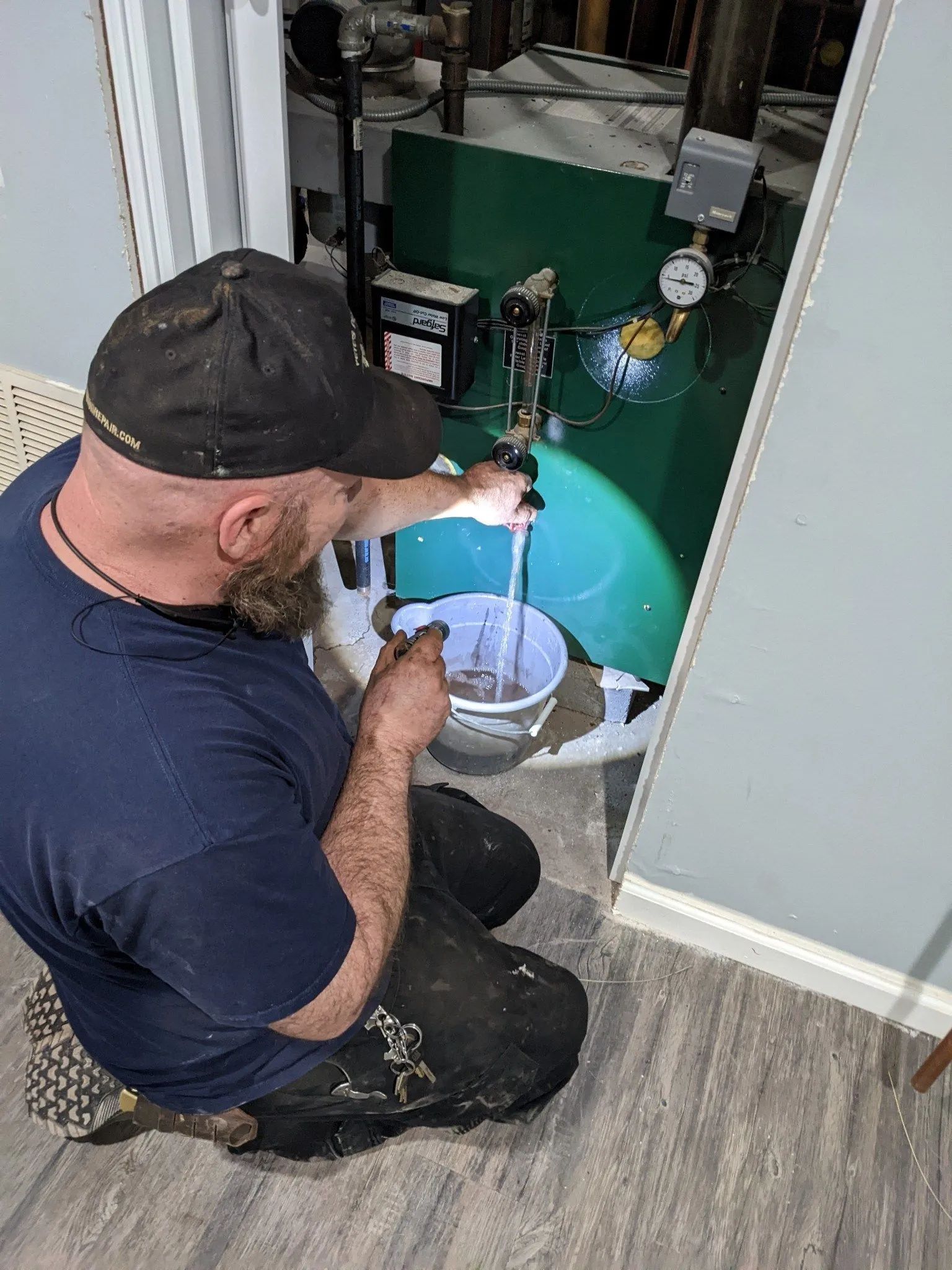 A man is kneeling down in front of a water heater.