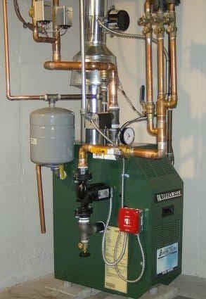 A green boiler with copper pipes attached to it is sitting in a room.