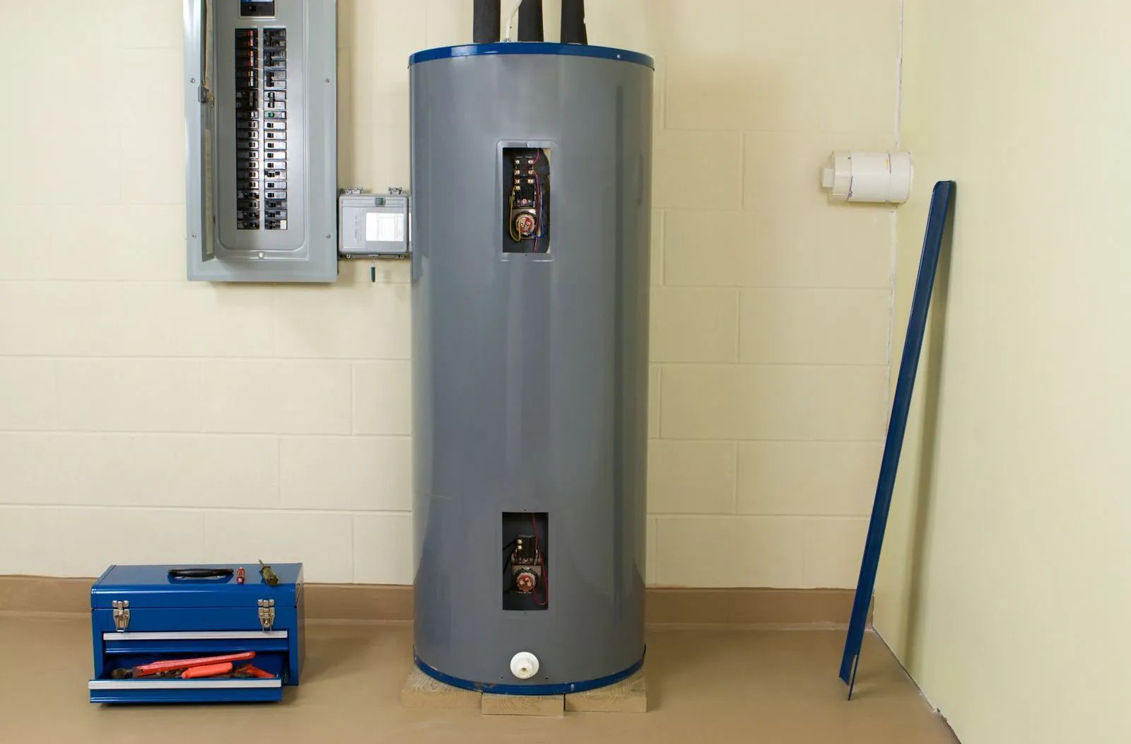 Utility room with a gray water heater, electrical panel, blue toolbox, and broom against a beige wall.