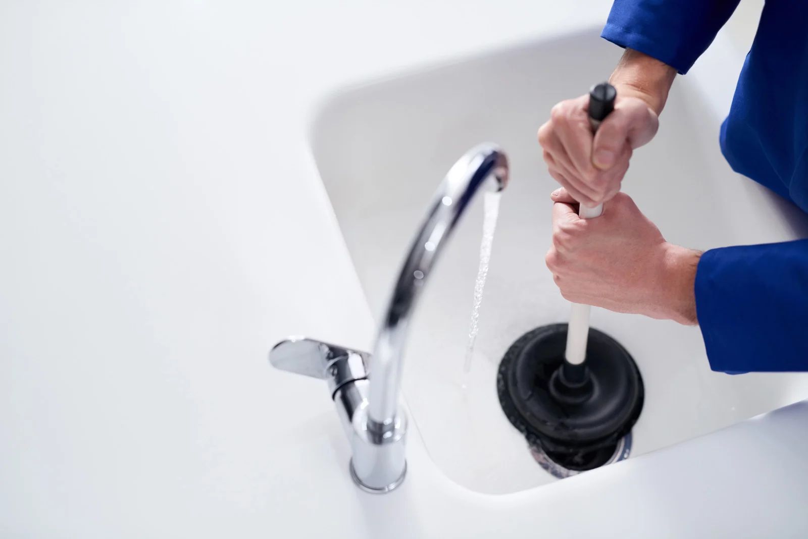 Hands unclog a bathroom sink with a plunger next to a silver faucet