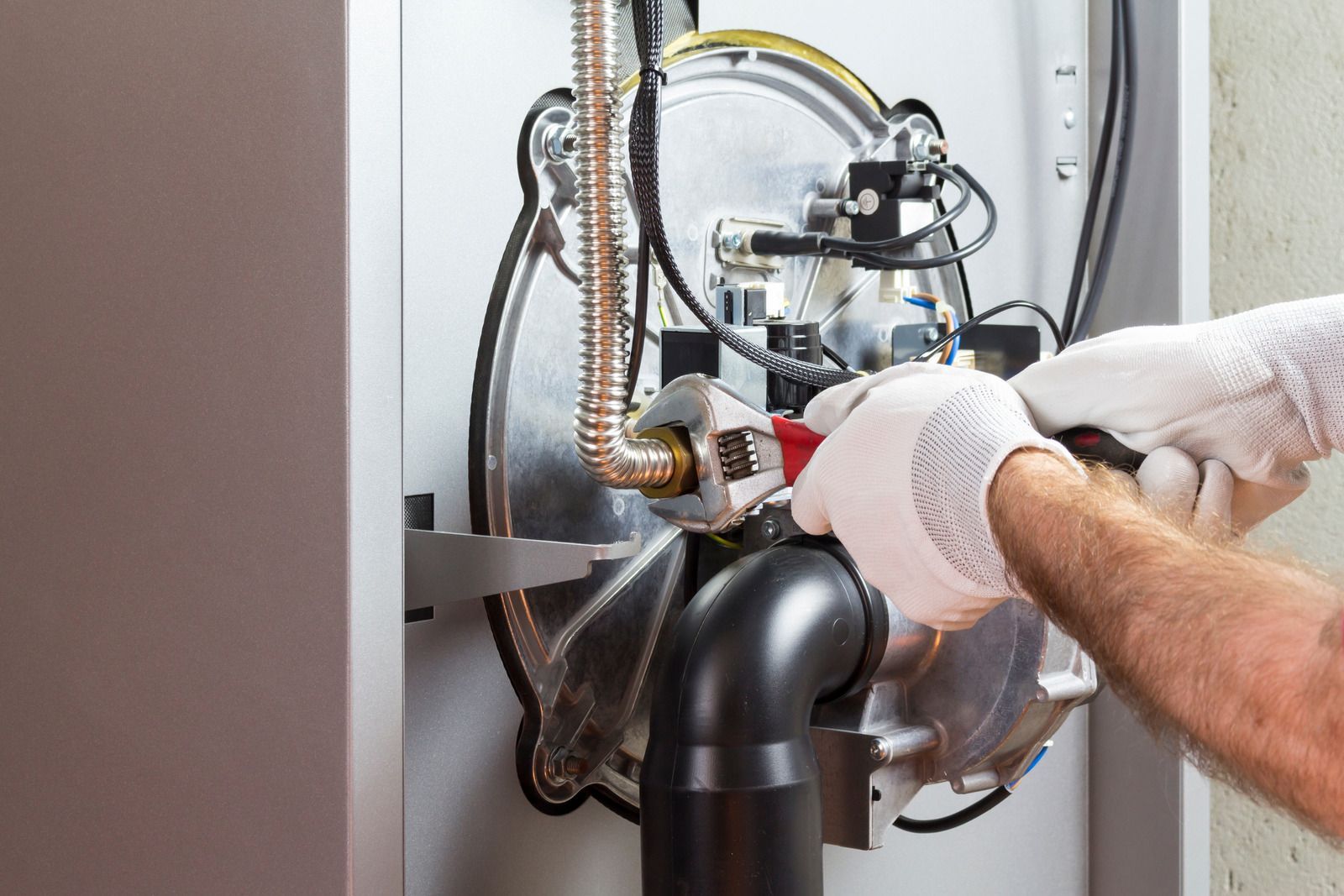 Gloved hands installing plumbing under a sink with pipes and fittings in a kitchen cabinet