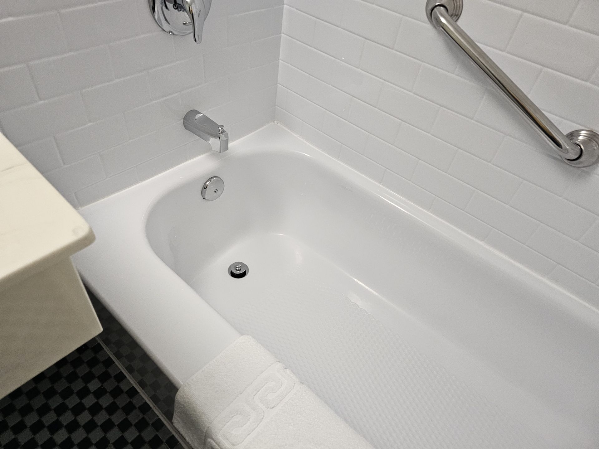 A white bathtub in a bathroom with a towel on the floor.