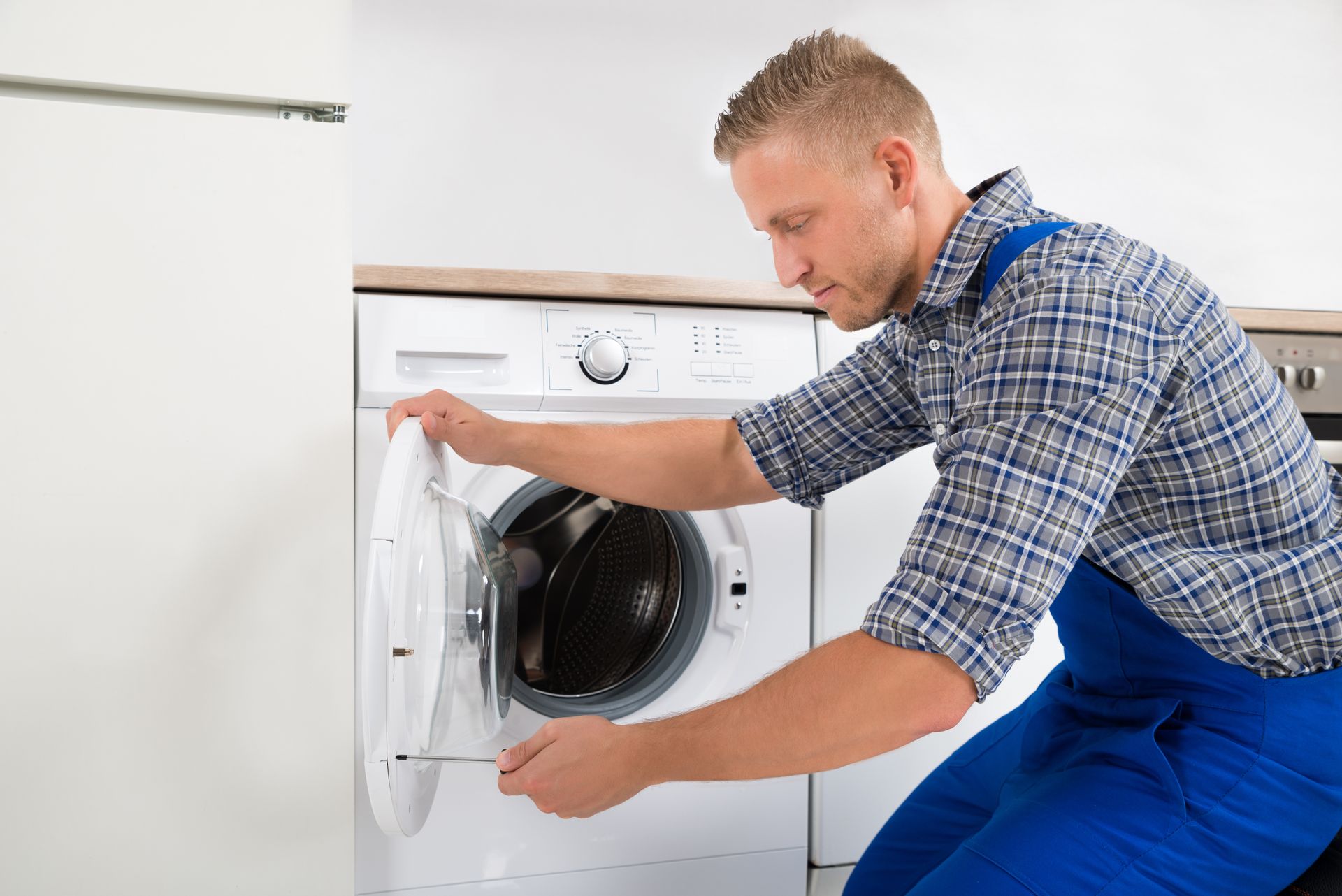 A man is fixing a washing machine in a kitchen.